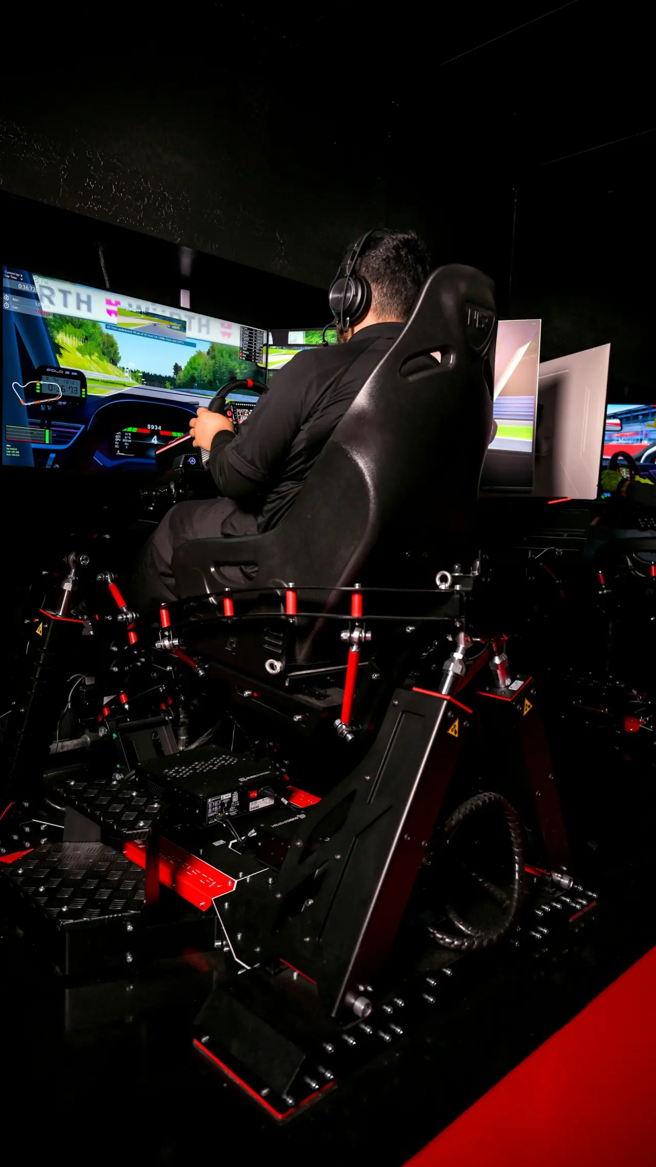 Çoklu ekranlı profesyonel sim racing kokpitinde yarış simülasyonu oynayan sürücü
